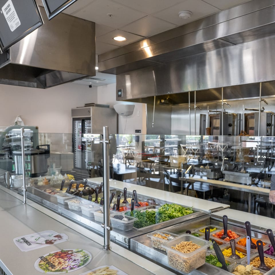 Natural Greens salad bar with fresh ingredients, toppings, and a view of the dining area.