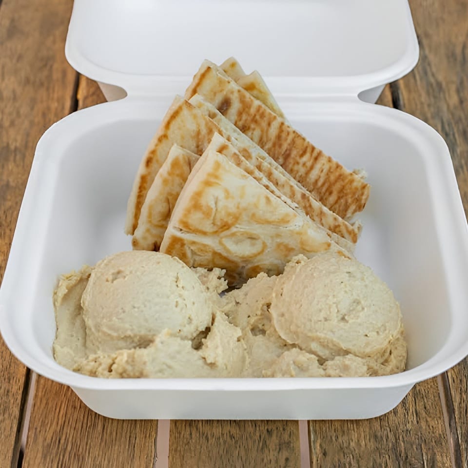 Hummus and pita bread in a white takeout container on a wooden table.
