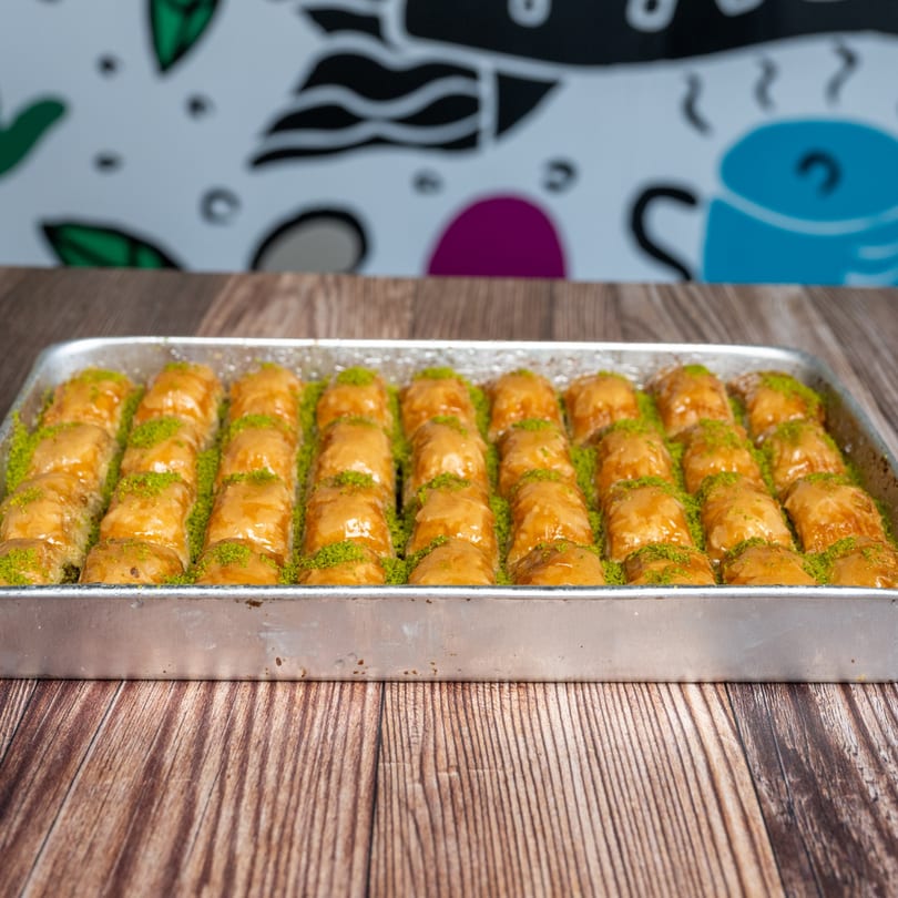 A tray of golden baklava rolls, drizzled with syrup and sprinkled with green pistachios.
