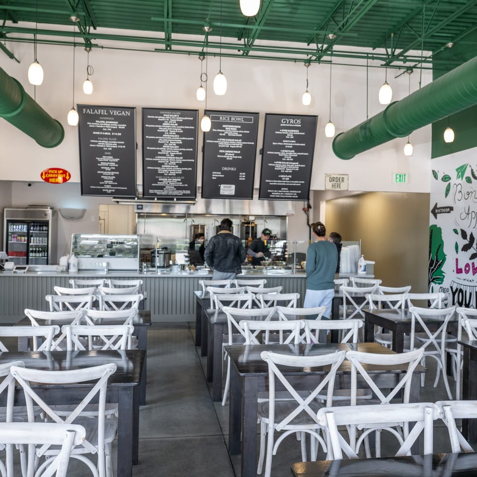 Interior of Natural Greens restaurant with customers ordering at the counter and empty dining tables.