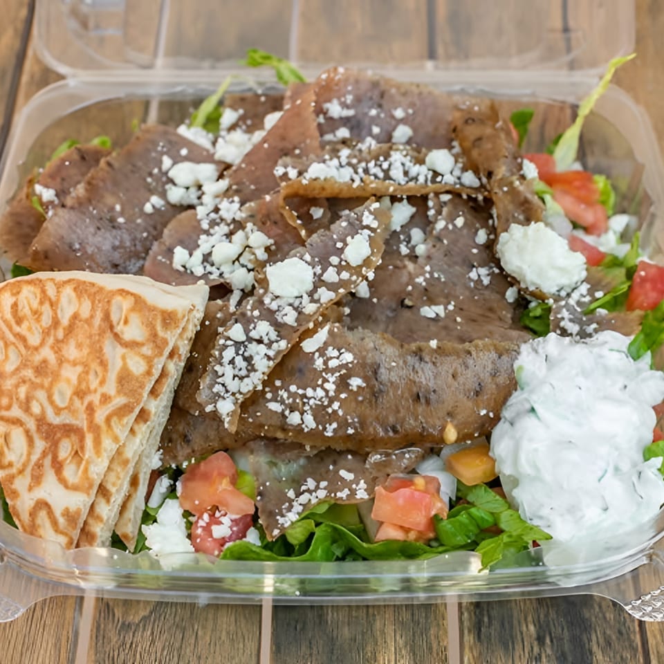 Natural Greens' Gyro Salad with sliced meat, feta, tomatoes, lettuce, tzatziki, and pita bread.