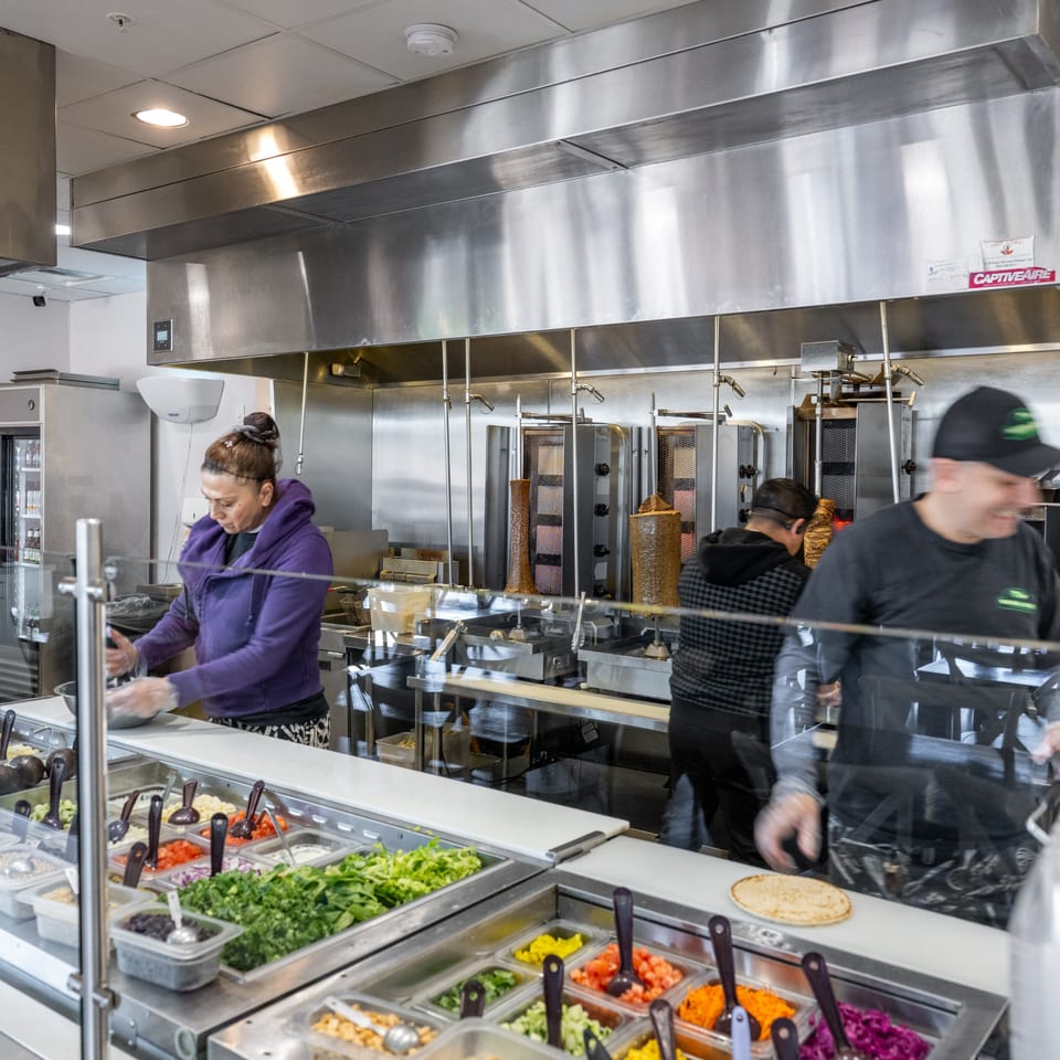 Natural Greens restaurant kitchen with staff preparing food behind a salad bar and shawarma machines.