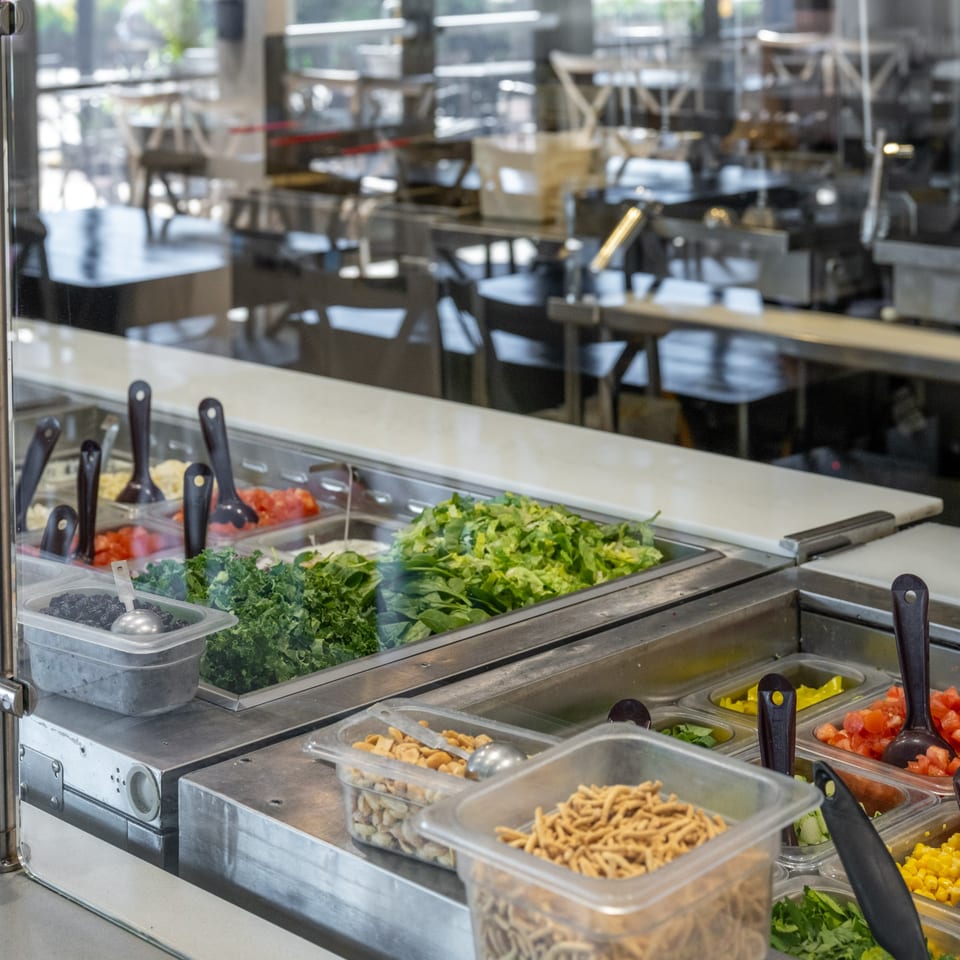 Salad bar at Natural Greens with fresh greens, toppings, and a blurred dining area in the background.